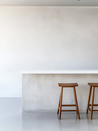 A spacious and modern kitchen features a sleek white counter and two wooden stools against a light-colored wall. The design emphasizes simplicity and a fresh uncluttered look.の素材