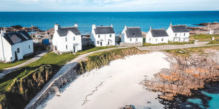 A row of quaint white cottages sits along a secluded beach surrounded by rugged cliffs and vibrant blue waters. The peaceful environment invites relaxation and exploration.の素材