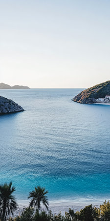 A tranquil coastal view showcases gentle waves lapping against rocky shores. The sun sets behind distant hills casting a warm glow over the peaceful waters and surrounding landscape.の素材