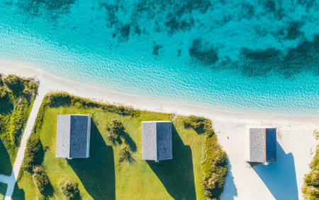 Cabins with wooden roofs are positioned along a pristine beach surrounded by lush greenery and crystal-clear water reflecting the vibrant colors of a sunny day in a tropical paradise.の素材