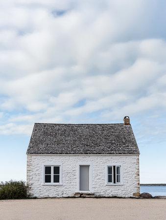 A quaint white house sits alone along the coastline framed by a vast sky filled with fluffy clouds. Its simple architecture complements the serene seaside atmosphere.の素材