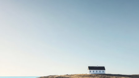 A solitary white house stands on a grassy hill offering a view of the calm ocean waters during sunrise. The clear sky enhances the peaceful atmosphere around the structure.の素材