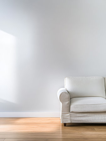 A simple white couch is placed in a bright minimalist room with a large window allowing sunlight to illuminate the space. The light wooden floor complements the decor.の素材