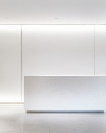 A sleek reception area features a minimalist white desk against a blank wall illuminated by soft lighting. This design emphasizes cleanliness and modern aesthetics.の素材
