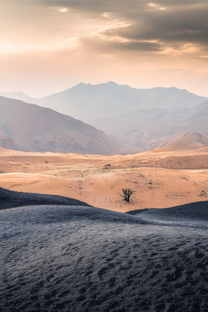 A vast desert stretches under a dramatic sky as the sun sets casting warm hues on the sand dunes. Distant mountains create a stunning backdrop against the horizon.の素材