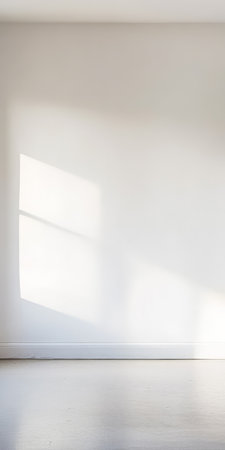 Soft sunlight filters through a window creating gentle shadows on a clean white wall. The minimalist setting evokes a sense of calm and spaciousness inviting tranquility.の素材