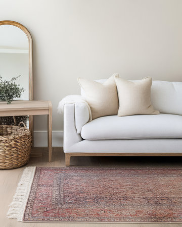 A stylish living room showcases a white sofa adorned with neutral pillows. A mirror is mounted on the wall above a wooden table with a textured rug beneath creating a warm and inviting atmosphere.の素材