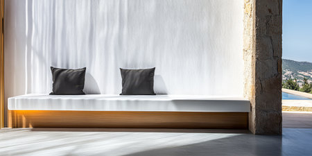 A modern seating space features a sleek white bench with two dark cushions bathed in soft light. The backdrop shows a serene landscape suggesting a peaceful start to the day.の素材