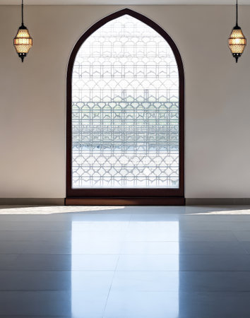 Soft light filters through a beautifully designed arched window adorned with intricate patterns and two hanging lanterns creating a peaceful ambiance in a spacious interior.の素材