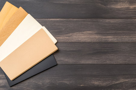 Several material samples in different colors are spread out on a dark wooden surface. These samples are commonly used for interior design or renovation projects showcasing various textures and tones.の素材