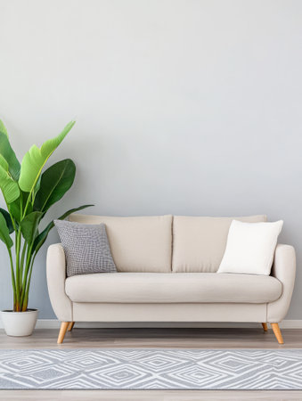 A modern beige sofa sits against a light gray wall complemented by two decorative cushions. A green indoor plant in a pot enhances the cozy atmosphere of the room.の素材