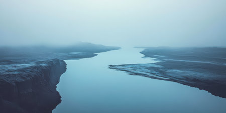 A serene river flows through a rugged landscape shrouded in thick fog during early morning. The muted colors create a tranquil and mysterious atmosphere.の素材