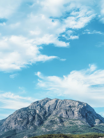 A stunning view of a large mountain showcases its rocky texture beneath a clear blue sky dotted with fluffy clouds. The natural beauty creates a serene and peaceful atmosphere.の素材