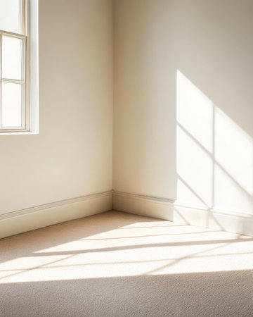 Soft sunlight filters through a window casting gentle shadows on a beige carpet in a minimalistic corner of a room. The light creates a serene and calming atmosphere.の素材