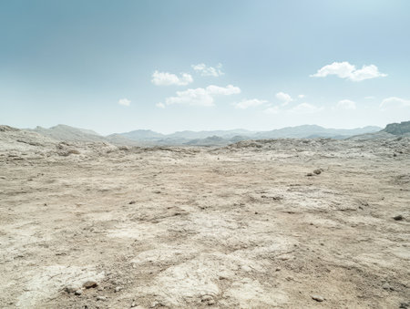 Expansive dry land stretches under a bright sky with few clouds. The ground shows cracks and textures indicating arid conditions. Mountainous formations are visible in the distance.の素材