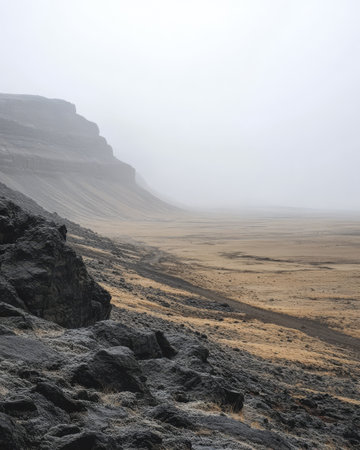Fog envelops a vast landscape characterized by rocky cliffs and stretches of barren land. The early morning light casts a soft glow over the unique terrain creating an ethereal atmosphere.の素材