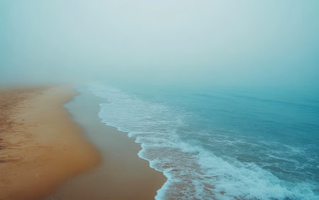 A tranquil beach landscape shows gentle waves lapping against a sandy shore surrounded by a thick mist. The early morning atmosphere creates a serene and peaceful environment.の素材