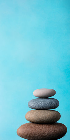 A serene arrangement of smooth stones stacked in various soft hues of gray brown and beige set against a tranquil blue background. This composition promotes a sense of calmness.の素材