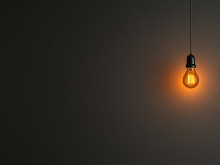 A warm light bulb hangs from an industrial-style fixture casting a soft orange glow in a dark environment. The simplicity of the design creates an inviting atmosphere.の素材