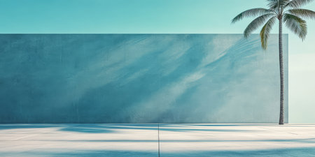 Bright and colorful tropical setting showcases a single palm tree standing beside a large smooth wall. Sunlight casts soft shadows on the pavement creating a serene atmosphere.の素材