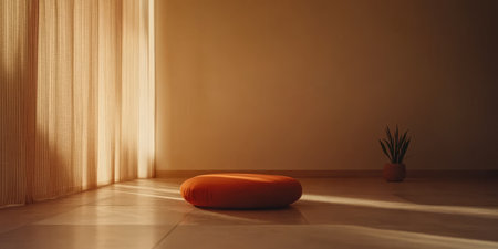 A soft orange cushion rests on a tranquil floor illuminated by warm natural light streaming through sheer curtains. A small plant adds a touch of nature to the peaceful setting.の素材
