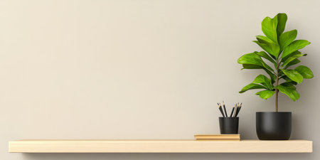 A minimalist shelf displays a leafy green plant in a black pot a small black container holding writing utensils and a stack of books. The soft light highlights the simplicity of the arrangement.の素材