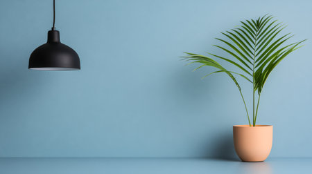 A potted palm sits on a light blue table with a calm blue wall behind. A stylish black pendant lamp hangs above creating a serene and contemporary atmosphere in the space.の素材
