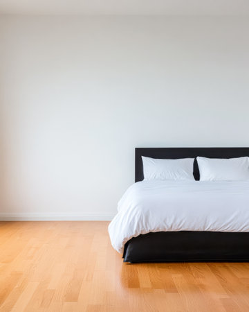 A spacious bedroom showcases a black bed with white pillows and a comforter. Natural light fills the room highlighting the wooden floor and simple decor creating a calm atmosphere.の素材