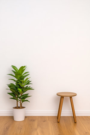 A vibrant green indoor plant stands in a white pot beside a simple wooden stool in a bright minimalistic interior. The scene highlights clean lines and natural materials.の素材