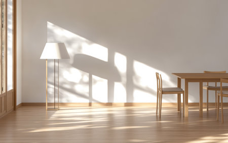 Sunlight streams through large windows casting intricate shadows of leaves on the wooden floor. A simple table and chairs complement the elegant lamp creating a serene atmosphere.の素材