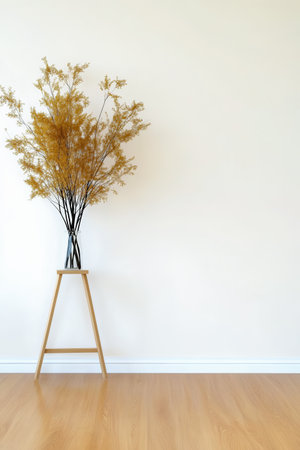 A stylish arrangement of dried yellow flowers in a glass vase stands on a wooden stool against a light wall. The warm wooden floor enhances the minimalist decor of the space.の素材