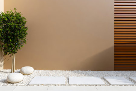 A minimalistic outdoor area showcases a smooth beige wall a small tree and smooth stones laid on white gravel. The design emphasizes simplicity and modern aesthetics in landscaping.の素材