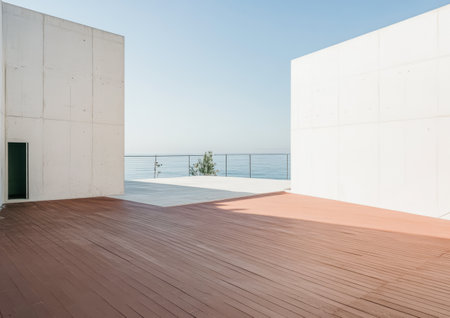 A minimalist white concrete structure is positioned near the ocean. The wooden deck captures sunlight creating a tranquil outdoor space. The clear sky enhances the peaceful atmosphere.の素材
