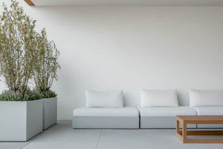 Clean and spacious interior featuring a white minimalist couch paired with a wooden coffee table. Lush green plants sit in large planters adding a touch of nature to the modern design.の素材