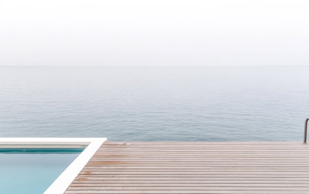A wooden deck extends towards calm ocean waters under a subdued sky. The tranquil scene invites relaxation with soft colors reflecting the serenity of nature and a minimalist design.の素材