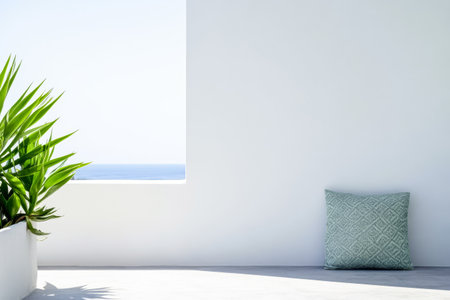 A serene outdoor area features a minimalist design with a green plant and a decorative pillow placed against a white wall overlooking a beautiful ocean view under clear blue skies.の素材