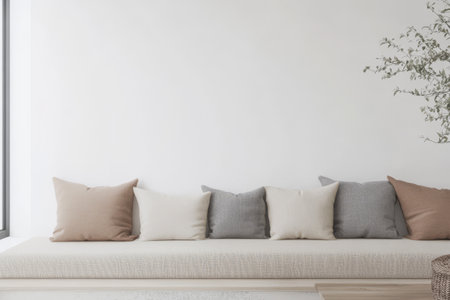 A minimalist living area features a long soft couch adorned with cushions in beige and gray shades. An elegant plant adds a touch of nature against the clean white wall.の素材