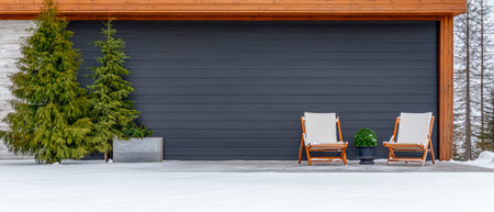Two elegant wooden chairs sit on a snow-covered surface beside a modern garage adorned with lush greenery. The winter scene showcases the tranquil beauty of a snowy day.の素材