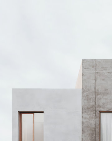 A contemporary building showcases a blend of concrete and white surfaces emphasizing geometric shapes and simplicity set against a cloudy sky.の素材