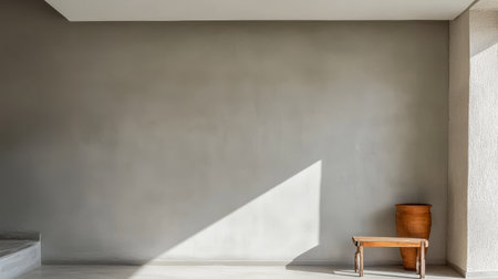 A spacious room is illuminated by natural light highlighting the smooth gray wall. A simple wooden bench sits beside a terracotta pot creating a calm and airy atmosphere.の素材
