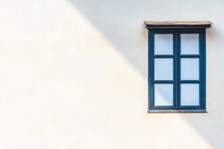 A blue window with four panes sits on a neutral white wall casting soft shadows in the afternoon sun. The simplicity of the design highlights the architectural beauty.の素材