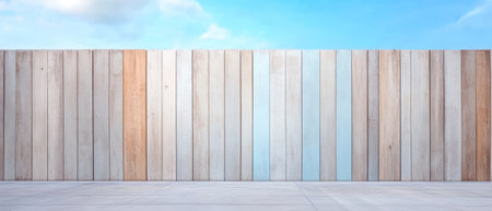 A colorful wooden fence made of varying shades of wood stands against a clear blue sky. Soft clouds drift in the background creating a peaceful outdoor atmosphere.の素材