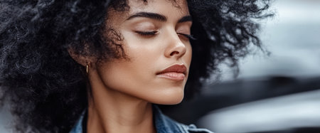 A young woman with voluminous curly hair closes her eyes embracing a peaceful moment amidst the hustle of the city.の素材