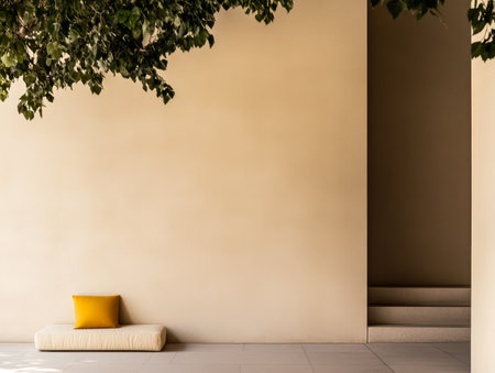 A serene outdoor area features a beige wall soft seating with a yellow pillow and a staircase leading to an unseen space. The greenery above adds tranquility to the minimalist design.の素材
