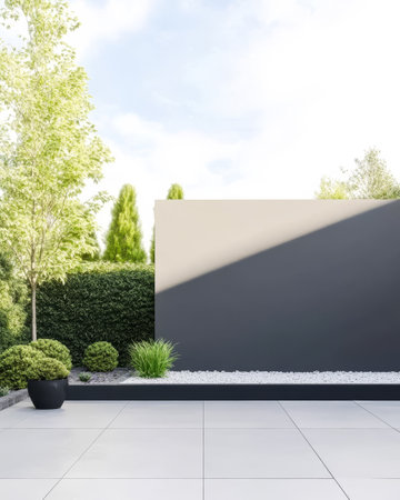 A contemporary garden layout showcases neatly arranged greenery including shrubs and ornamental grasses against a minimalist wall. Sunlight highlights the fresh landscape.の素材