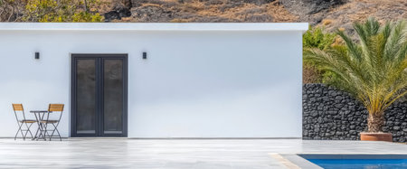 A sleek white building stands beside a serene pool with a small patio set featuring two chairs and a table. Lush greenery and stone walls create a tranquil atmosphere in bright sunlight.の素材