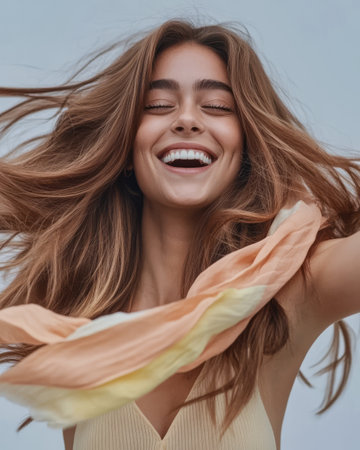 A young woman with long flowing hair laughs joyfully her hair and a light scarf swirling around her. She exudes happiness against a backdrop of soft blue tones embodying a carefree spirit.の素材