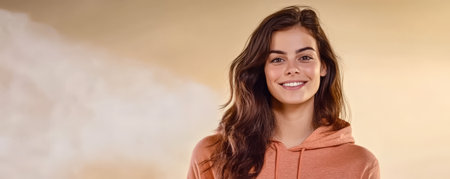 A young woman with long dark hair smiles warmly while wearing an orange hoodie. The background features soft golden hues typical of sunset creating a cozy atmosphere.の素材
