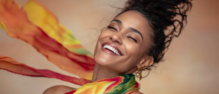 A woman smiles widely while wearing a colorful scarf that flows around her as she enjoys a moment of happiness. The warm background enhances her joyful expression creating a festive vibe.の素材