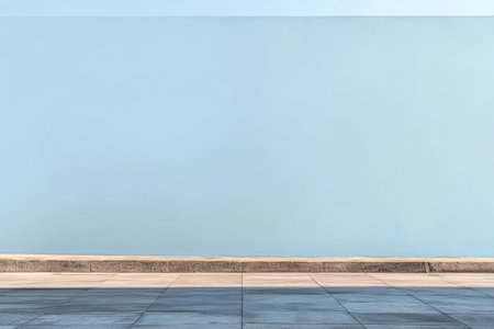 A smooth bright blue wall stretches along a clean well-kept sidewalk under a clear blue sky. Sunlight bathes the scene enhancing the calm urban atmosphere.の素材